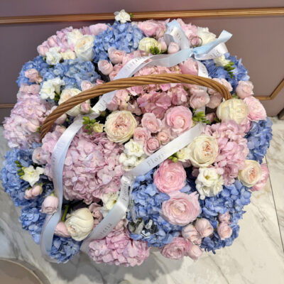 Блакитно рожева композиція в корзині з ранункулюсами та піоновидними трояндами