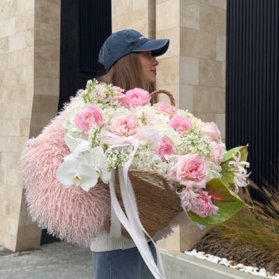 Композиція в плетеній сумці з ранункулюсів, троянд, бузку, орхідей, наріне та антуріуму