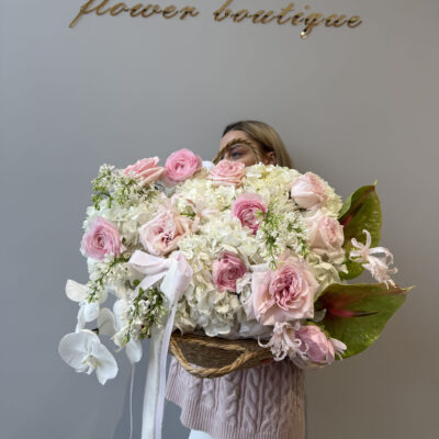 Композиція в плетеній сумці з ранункулюсів, троянд, бузку, орхідей, наріне та антуріуму